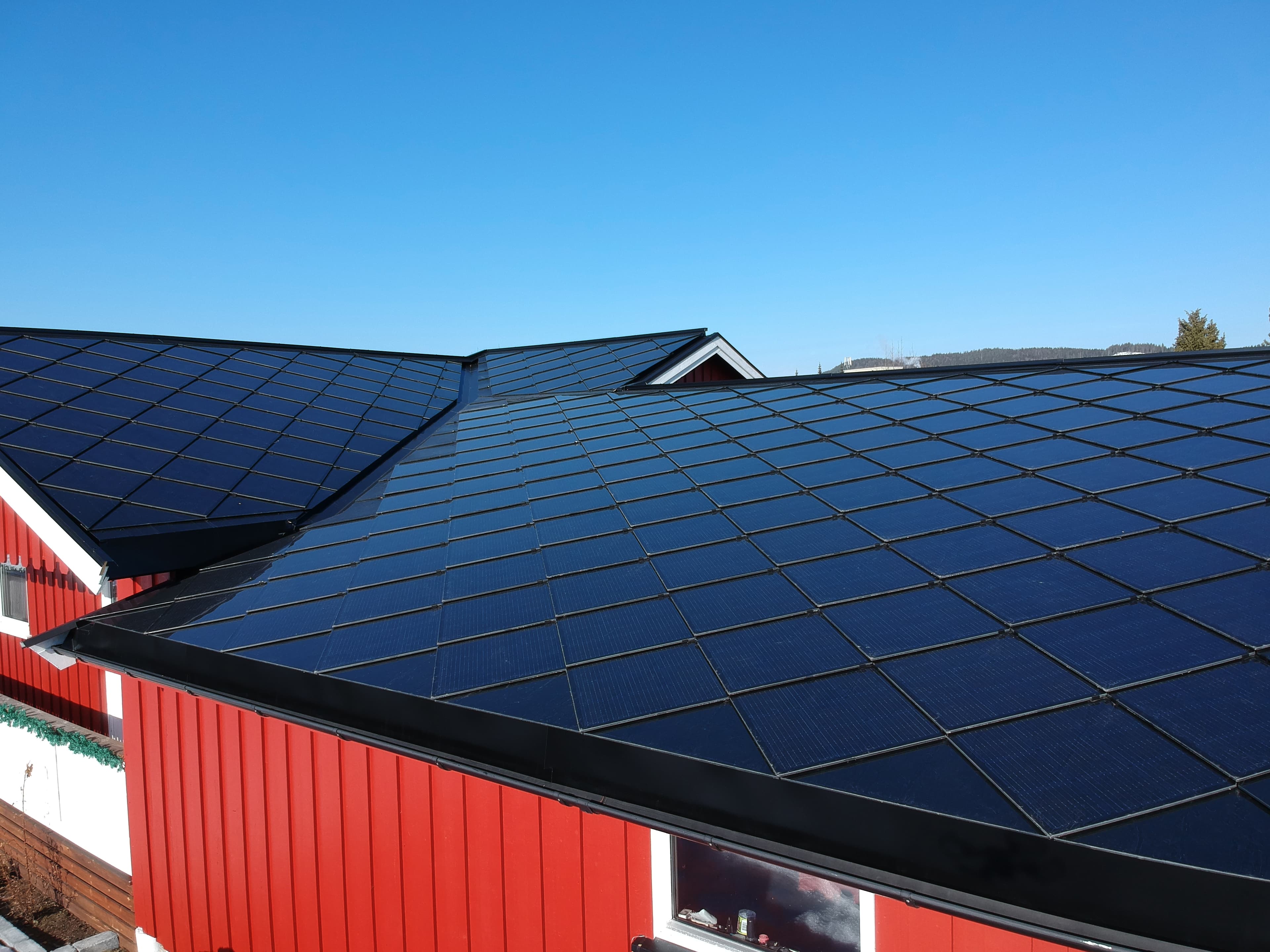 Rødt hus med Solskifer solcelletak i diamantmønster mot blå himmel
